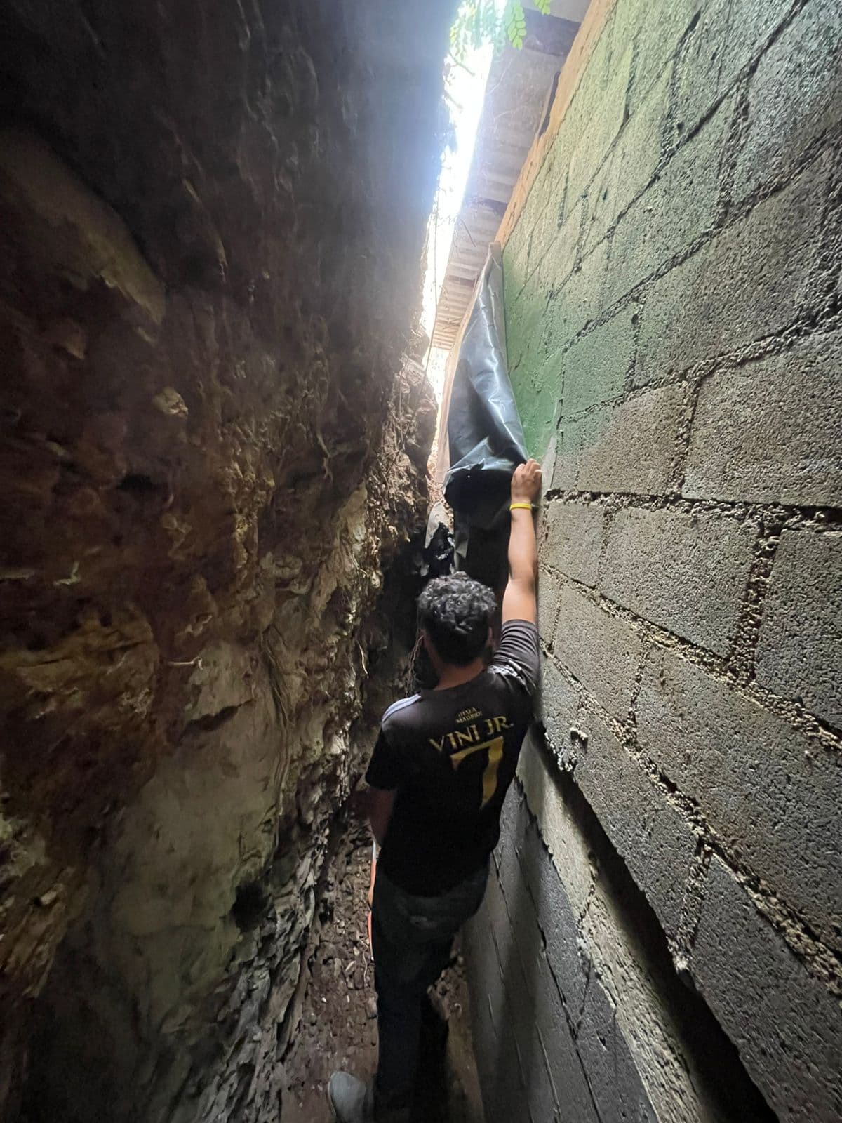Construction worker managing a tarp in a narrow excavation space.